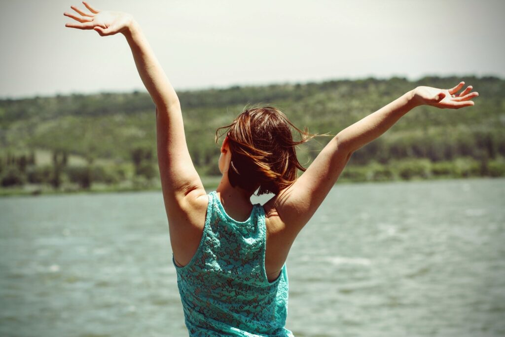 woman standing in front of river with arms open wide
