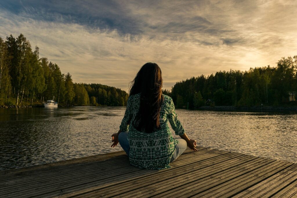 woman meditates on dock overlooking lake